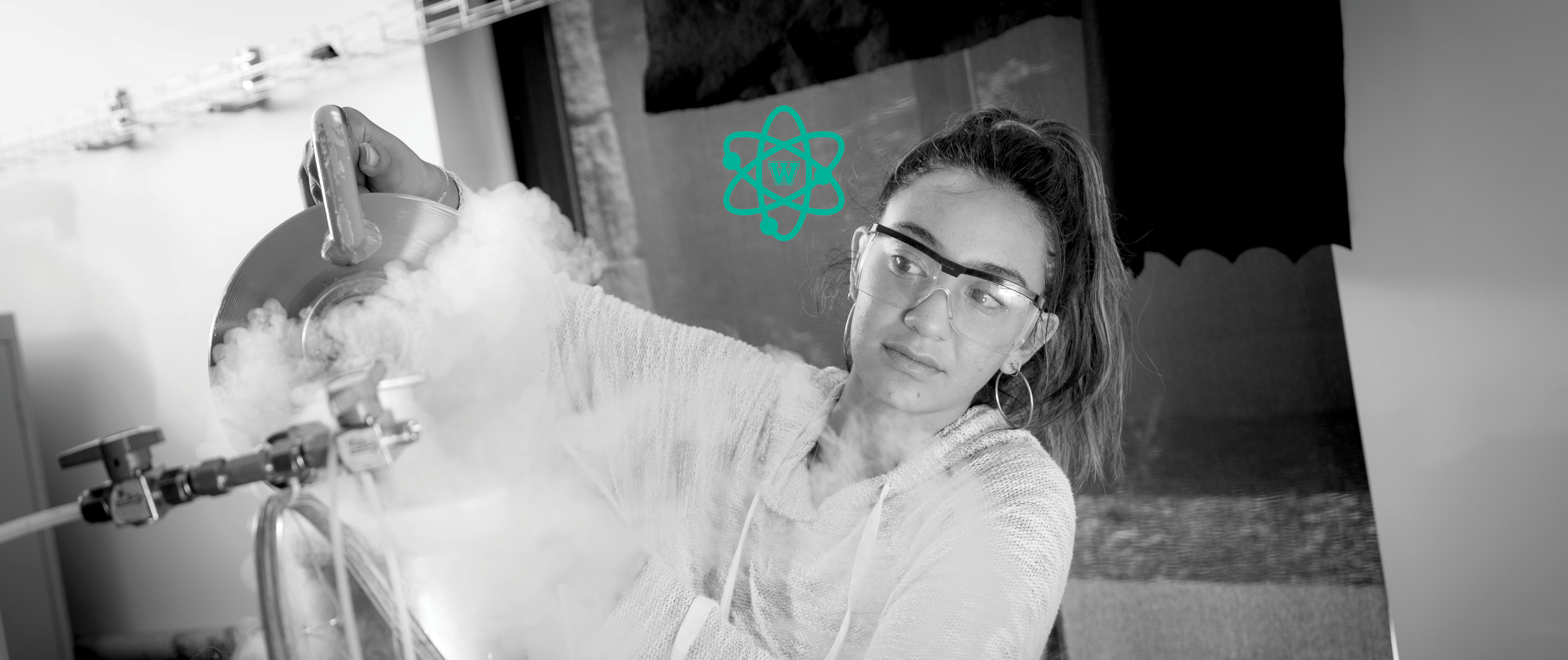 black & white image of female student wearing safety goggles working in lab; Westmont STEM icon above.