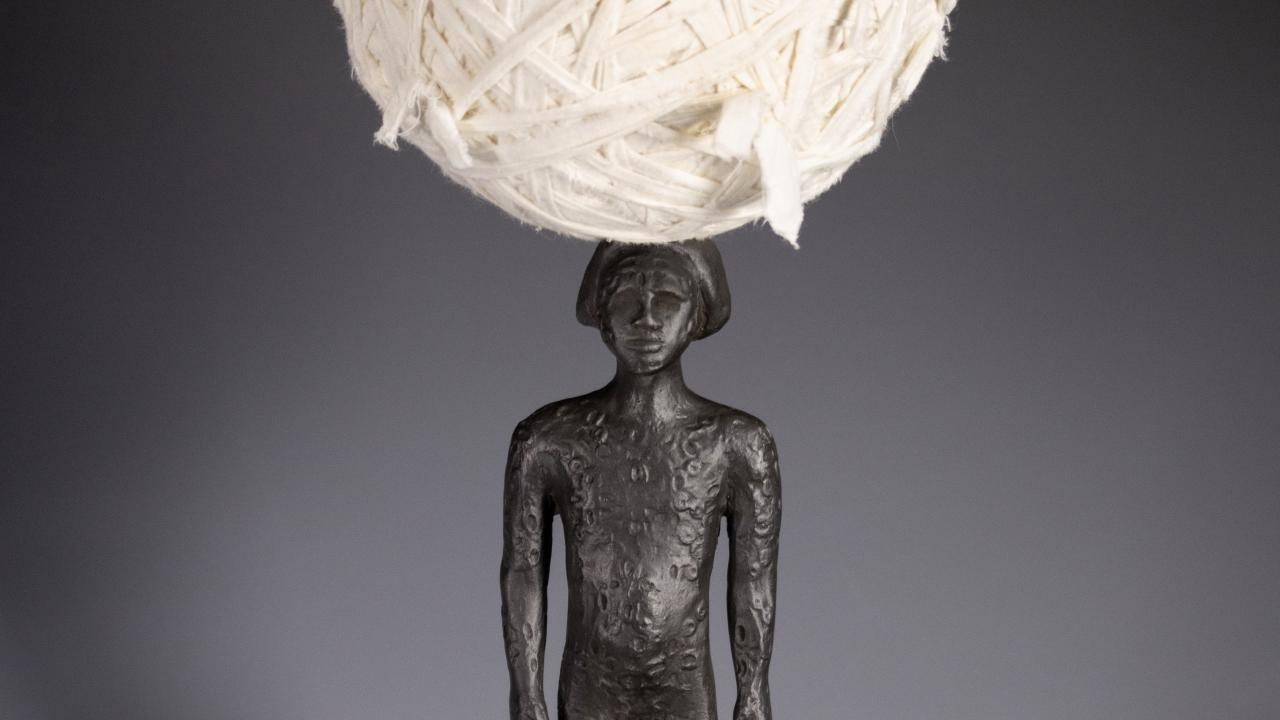 Bronze female figure with large ball of white cotton balanced on her head.