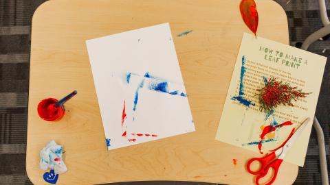 Craft station with paint, leaves, and instructions on how to make a leaf print artwork.