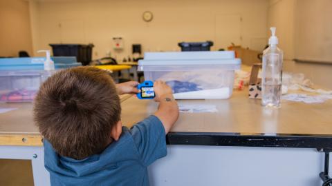 A young boy taking a photo of a snake in a clear box.