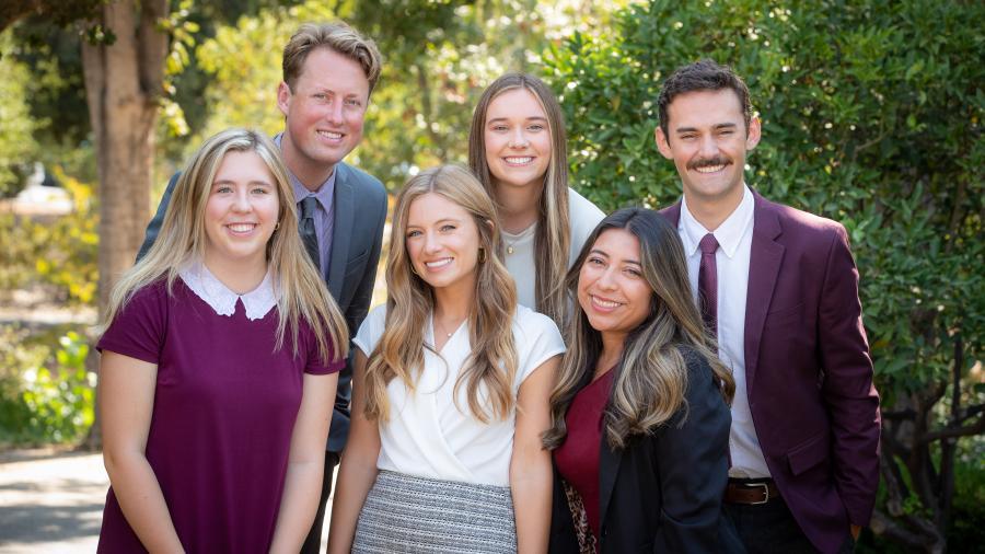 Group of 2 men and 4 women dressed nicely, smiling at the camera.