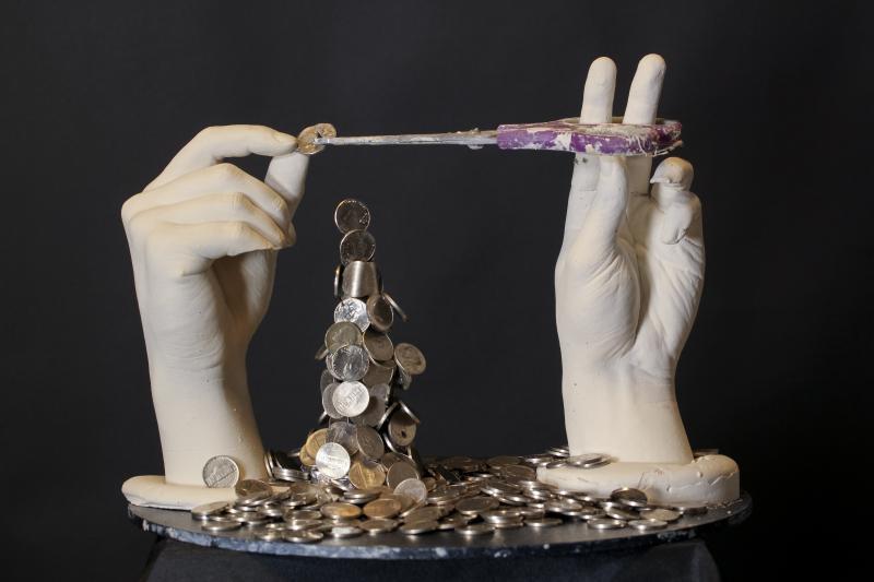 two plaster hands with scissors cutting a coin and nickels piled underneath