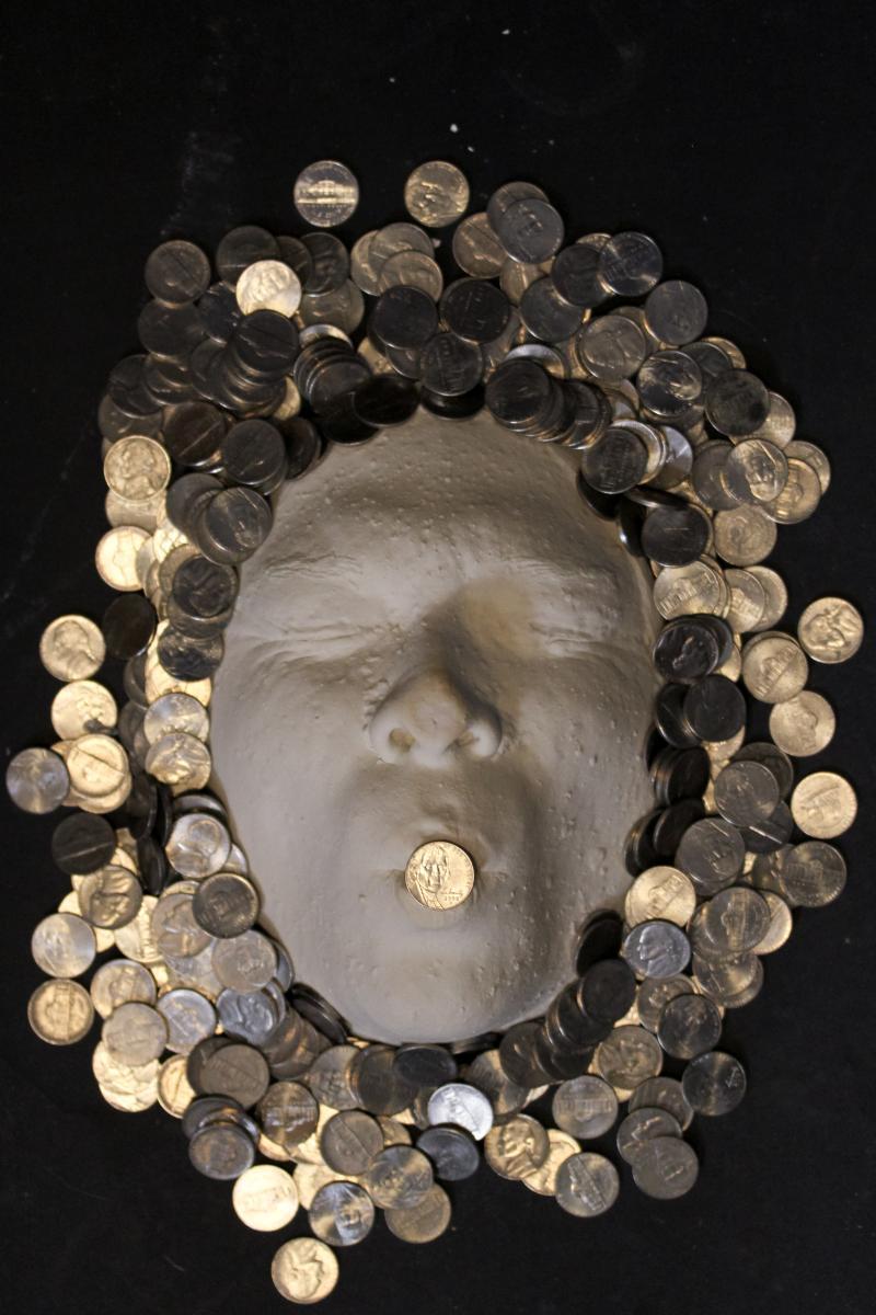 plaster face surrounded by nickels with one nickel over the mouth