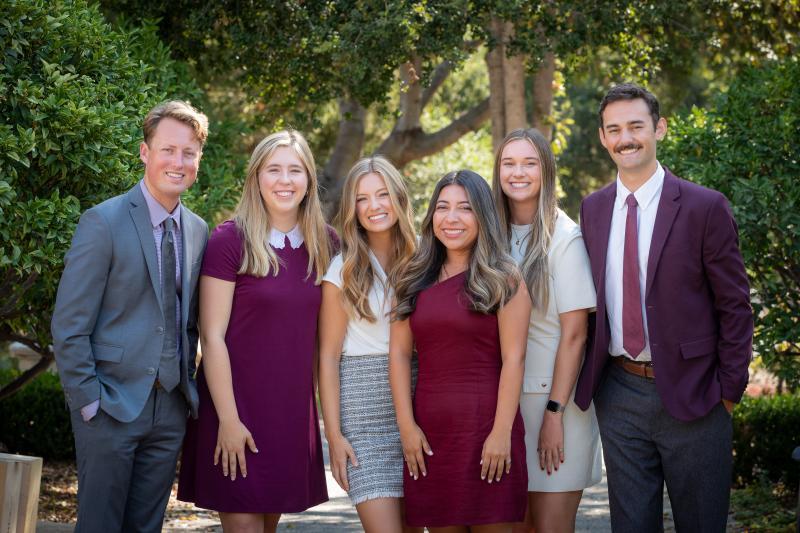 Group of two young men and four young women in business attire, smiling at the camera.